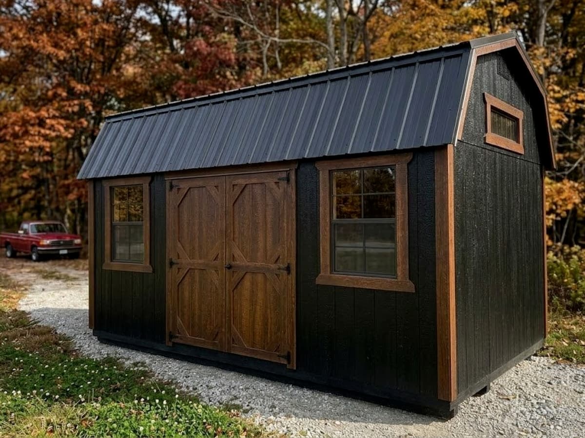 Black Lofted Barn with stained wood doors and window trim on a gravel pad