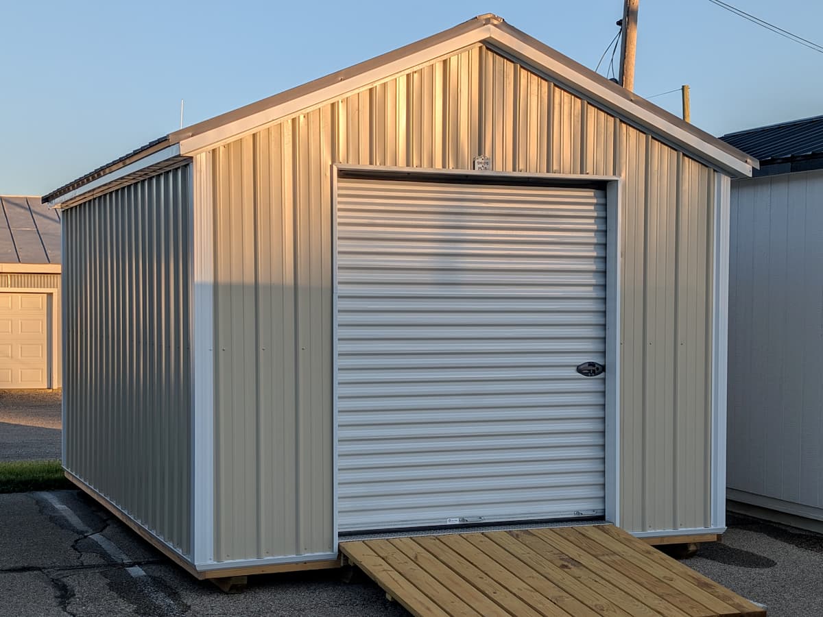 Gable Garage with tan metal siding and white roll-up door with wooden ramp